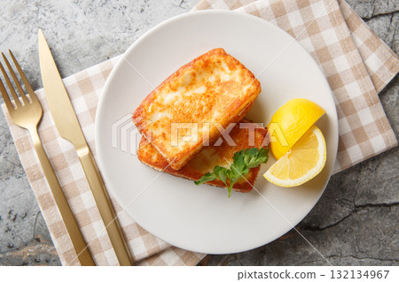 Saganaki is a very popular Greek appetizer of pan-seared cheese served alongside lemon wedges close-up in a plate. Horizontal top view 132134967