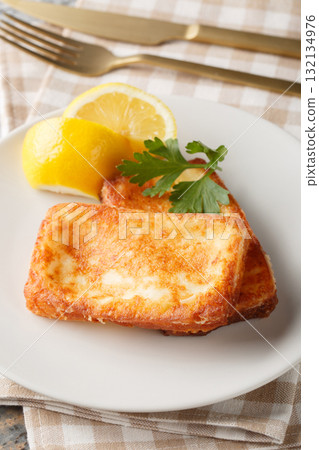Saganaki is a Greek appetizer consisting of pan-fried cheese served with a lemon wedge, close-up on a plate. Vertical Saganaki is a Greek appetizer consisting of pan-fried cheese served with a lemon wedge, close-up on a plate. Vertical 132134976