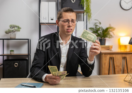 Upset young businessman freelancer counting dollar cash insufficient amount of money at office desk Upset young businessman freelancer counting dollar cash insufficient amount of money at office desk 132135106