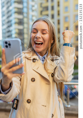 Happy businesswoman using smartphone celebrating victory win message news on downtown city street 132135133