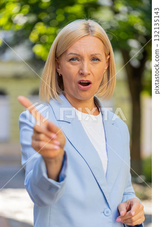 Caucasian mature businesswoman in suit standing in city street looking at camera shaking finger Caucasian mature businesswoman in suit standing in city street looking at camera shaking finger 132135143