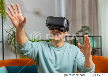 Asian man use virtual reality headset typing virtual keyboard play simulation 3D video game at home 132135145