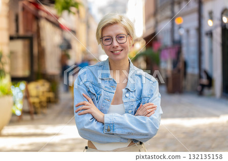 Portrait of happy Caucasian young woman looking at camera standing arms crossed on street Portrait of happy Caucasian young woman looking at camera standing arms crossed on street 132135158