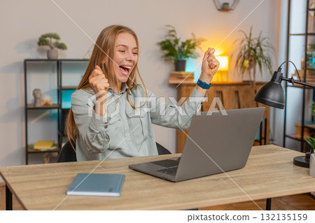 Excited Caucasian woman working on laptop shocked by sudden victory sitting at home office desk 132135159