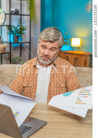 Mature man sitting at table with laptop and documents showing financial distress bankruptcy at home Mature man sitting at table with laptop and documents showing financial distress bankruptcy at home 132135195