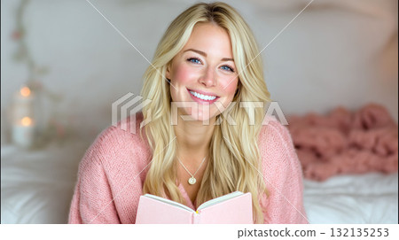 Smiling young woman in pink sweater reading a book while sitting comfortably on a bed in cozy home interior Smiling young woman in pink sweater reading a book while sitting comfortably on a bed in cozy home interior 132135253