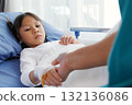 asian girl patient lying in hospital bed with bandaged hand and IV line, holding hands with nurse, doctor, medical professional or father. healthcare with compassion, trust and emotional support. 132136086