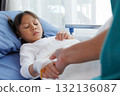 asian girl patient lying in hospital bed with bandaged hand and IV line, holding hands with nurse, doctor, medical professional or father. healthcare with compassion, trust and emotional support. 132136087
