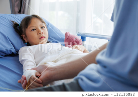 asian girl patient lying in hospital bed with bandaged hand and IV line, holding hands with nurse, doctor, medical professional or father. healthcare with compassion, trust and emotional support. asian girl patient lying in hospital bed with bandaged hand and IV line, holding hands with nurse, doctor, medical professional or father. healthcare with compassion, trust and emotional support. 132136088