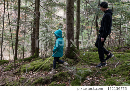 Exploring a tranquil forest trail with a child during autumn, surrounded by lush greenery and fallen leaves under a soft natural light Exploring a tranquil forest trail with a child during autumn, surrounded by lush greenery and fallen leaves under a soft natural light 132136753