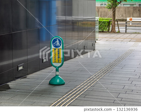 A sign stand placed on the premises of a commercial facility reads, "Please push your bicycle while walking." 132136936