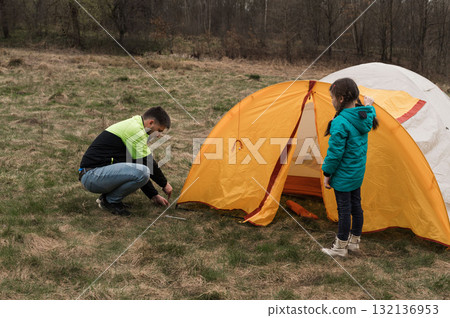 Enjoying quality time in nature while setting up a colorful tent with a child in a serene meadow during a tranquil afternoon adventure Enjoying quality time in nature while setting up a colorful tent with a child in a serene meadow during a tranquil afternoon adventure 132136953