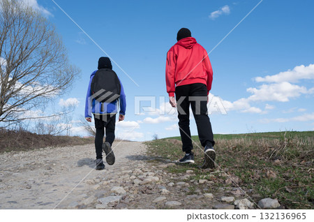 Two figures hike along a rocky path, under a bright blue sky. A journey of friendship and adventure. 132136965