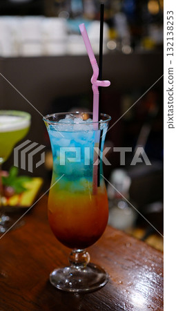 Colorful layered cocktail Refreshing layered cocktail in a tall glass with blue and yellow hues, topped with ice cubes and a red cherry, perfect for summer themes, parties, or drink menus. Colorful layered cocktail Refreshing layered cocktail in a tall glass with blue and yellow hues, topped with ice cubes and a red cherry, perfect for summer themes, parties, or drink menus. 132138253
