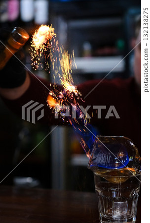 Male bartender holds fired up sugar above delicious alcohol cocktail 132138275
