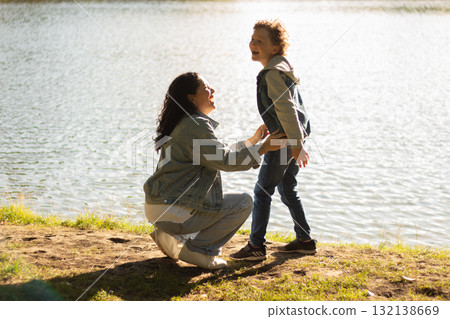 Mother and Son Enjoying Quality Time together by Serene Lake. Calm lake and golden sunlight create peaceful, loving atmosphere. Perfect for family bonding themes. High quality image 132138669
