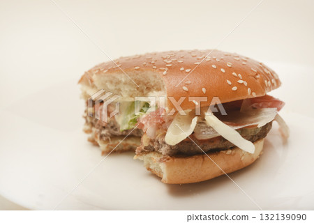 A nibbled hamburger with meat and vegetables. Fast food. Hamburger on a plate. Fast food scraps. A nibbled hamburger with meat and vegetables. Fast food. Hamburger on a plate. Fast food scraps. 132139090