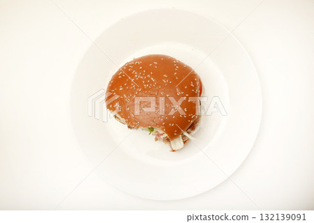 A nibbled hamburger with meat and vegetables. Fast food. Hamburger on a plate. Fast food scraps. 132139091