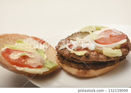 A nibbled hamburger with meat and vegetables. Fast food. Hamburger on a plate. Fast food scraps. A nibbled hamburger with meat and vegetables. Fast food. Hamburger on a plate. Fast food scraps. 132139099
