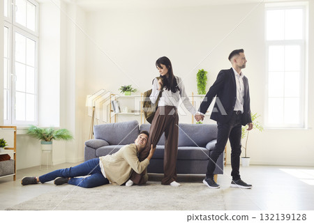 Dramatic scene with man clinging to woman leg as she walks away with another man Dramatic scene with man clinging to woman leg as she walks away with another man 132139128