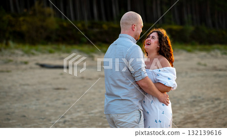 Couple enjoys a joyful moment on the beach during golden hour while looking into each other's eyes Couple enjoys a joyful moment on the beach during golden hour while looking into each other's eyes 132139616