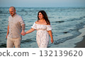 Couple walks hand in hand along the beach during sunset near the water 132139620