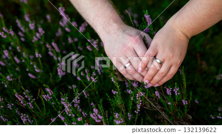 Couple's hands carefully gardening together in a lush green environment with pink flowers in the background Couple's hands carefully gardening together in a lush green environment with pink flowers in the background 132139622
