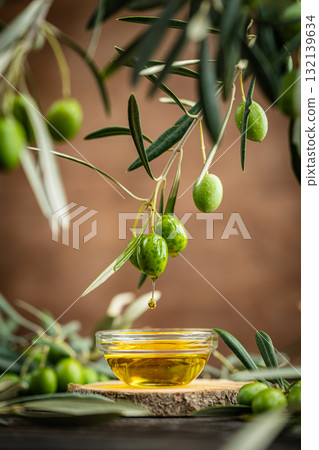 Bowl of olive oil with fresh green olives and olive branches on rustic wooden table 132139634
