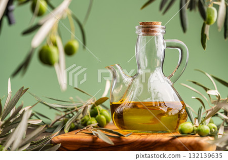 Glass bottle of olive oil surrounded by fresh olives and olive branches on wooden surface Glass bottle of olive oil surrounded by fresh olives and olive branches on wooden surface 132139635