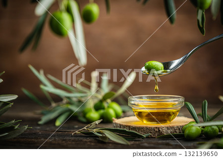 Pouring olive oil from spoon into glass bowl with olives and bottle on rustic table Pouring olive oil from spoon into glass bowl with olives and bottle on rustic table 132139650
