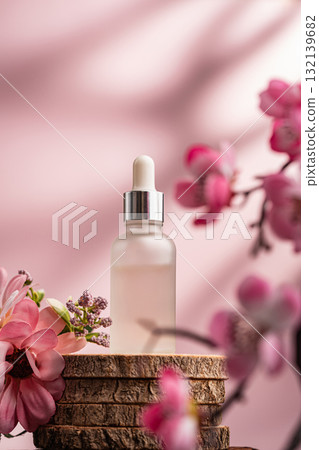 Glass serum bottle with dropper and pink flowers on wooden surface 132139682