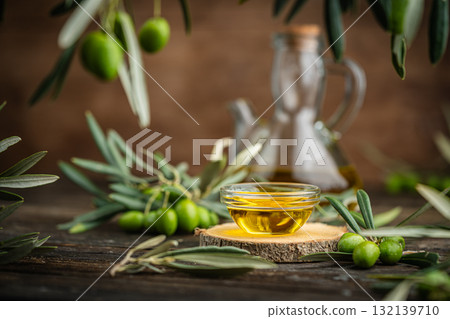 Glass bottle of olive oil with fresh green olives and olive branches on rustic table 132139710
