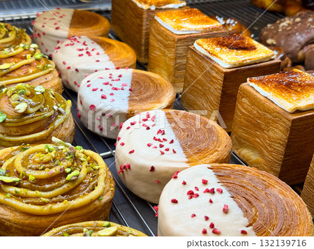 Pistachio rolls, round buns with icing, and caramelized cubes arranged on bakery rack. Dessert composition representing creativity, craft, and culinary art. 132139716