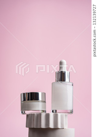 Anti-age serum and eye cream bottles on white stands with pink background 132139727