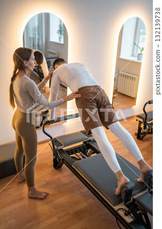 Woman Pilates Instructor Gives Guidance to a men Student While They Utilize the Reformers Equipment 132139738