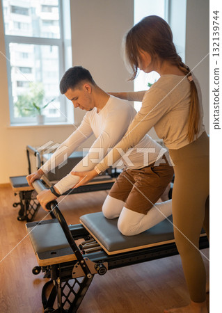 Woman Pilates Instructor Gives Guidance to a men Student While They Utilize the Reformers Equipment Woman Pilates Instructor Gives Guidance to a men Student While They Utilize the Reformers Equipment 132139744