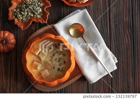 Creamy pumpkin soup with croutons and seeds, served in a pumpkin-shaped bowl on dark wooden table. Top view 132139797