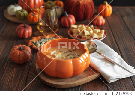 Creamy pumpkin soup with croutons and seeds, served in a pumpkin-shaped bowl on dark wooden table. 132139798