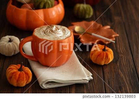 Cozy pumpkin latte in a pumpkin-shaped mug with whipped cream and spices, surrounded by autumn decor. 132139803