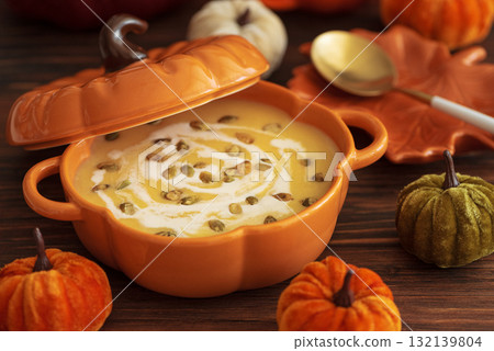 Autumnal lunch with pumpkin soup in a pumpkin-shaped bowl and festive decor on dark wooden table 132139804