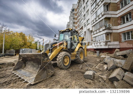 Construction equipment works on a building site with cloudy skies and autumn trees in the background Construction equipment works on a building site with cloudy skies and autumn trees in the background 132139896