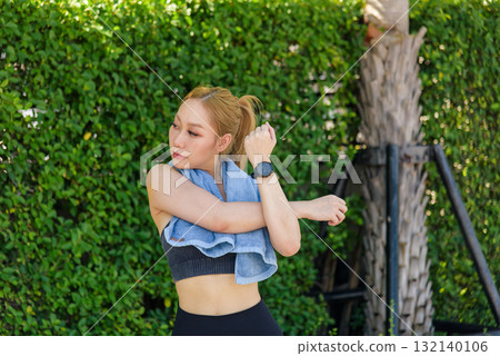 Sport woman exercise, fit young female performs arm stretch outdoor workout, people pursue active lifestyle, healthy sport activity, green foliage provides natural setting. 132140106