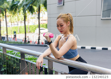 Fit woman performs focused outdoor sport workout exercising with pink dumbbell, developing strength for fit body, embracing active lifestyle in urban environment. Fit woman performs focused outdoor sport workout exercising with pink dumbbell, developing strength for fit body, embracing active lifestyle in urban environment. 132140123