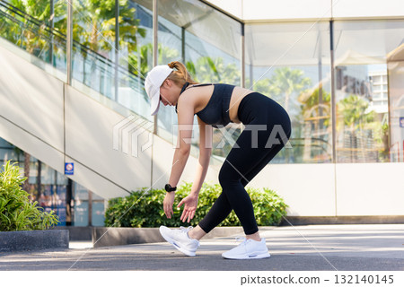 Exercise woman performs sport workout bending body for outdoor fitness, healthy people enjoy vigorous physical exercise in urban setting promoting well being. 132140145