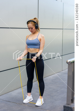 Fit woman enjoys outdoor sport exercise, wearing headphones for energizing workout, maintaining fit physique with resistance band, demonstrating dedicated people to healthy active lifestyle. Fit woman enjoys outdoor sport exercise, wearing headphones for energizing workout, maintaining fit physique with resistance band, demonstrating dedicated people to healthy active lifestyle. 132140160