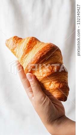 Beautiful Freshly Baked Croissant Held by a Hand Against a Light Background in a Cozy Setting 132140427