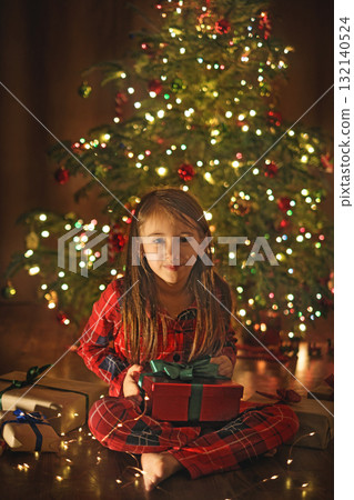 A cheerful laughing girl in the middle of the night curiously opens Christmas presents. 132140524
