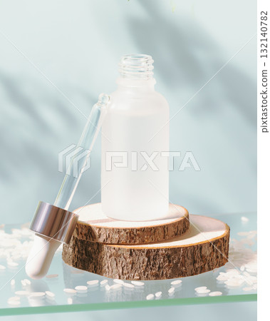 White glass dropper bottle with rise serum on a glass shelf with rise seeds on a blue background with shadows. Natural beauty product based on fermented products. Soft focus style White glass dropper bottle with rise serum on a glass shelf with rise seeds on a blue background with shadows. Natural beauty product based on fermented products. Soft focus style 132140782
