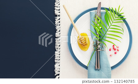 Rosh hashanah, Jewish New Year holiday. Rosh hashanah flat lay with table setting and traditional symbols, honey, and pomegranate seeds on white napkin on a blue background with copy space 132140785