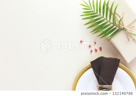 Holiday background. Present with palm leaf, table settings and pomegranate seeds on a beige background with copy space. Rosh hashanah, Jewish New Year holiday. Flat lay 132140786